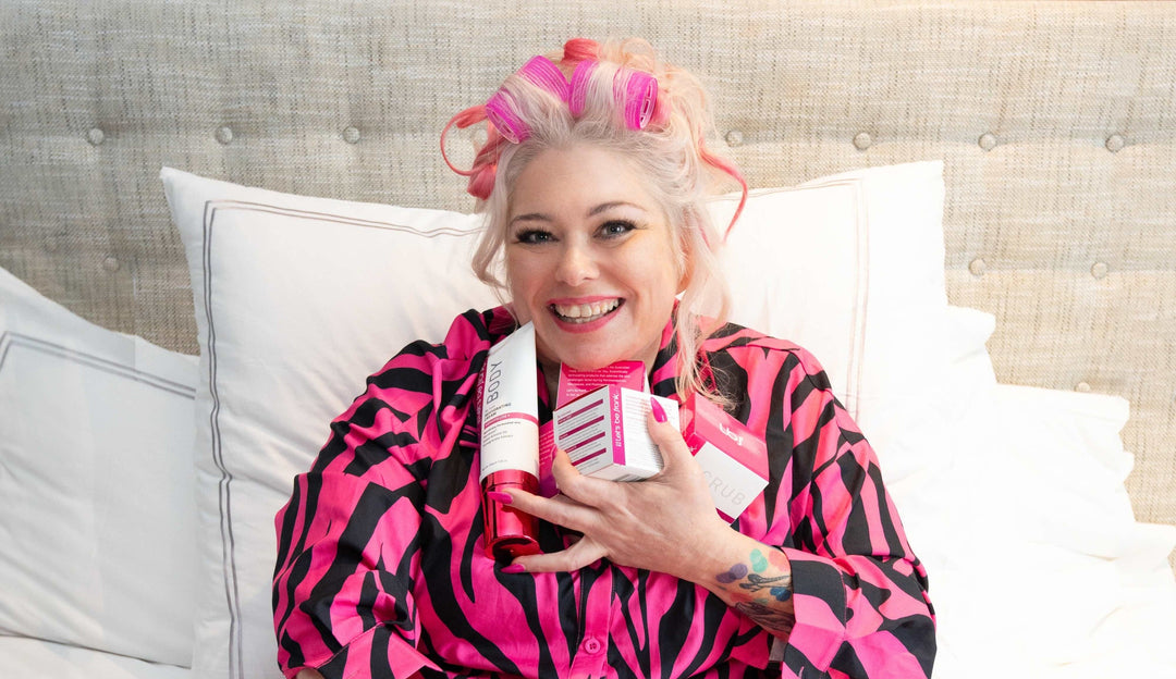 Person in a pink and black zebra print robe holding Let's be frank...skincare products on a bed.